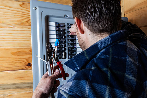 A close-up shot of a technician or handyman using wire strippers to prepare electrical cables for installation in a home circuit breaker box. Concept of home maintenance, electrical safety, and professional trade services.