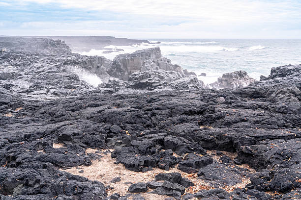 A stretch of coastline with black volcanic rocks and rough seas on the Reykjanes Peninsula in Iceland on a spring day.