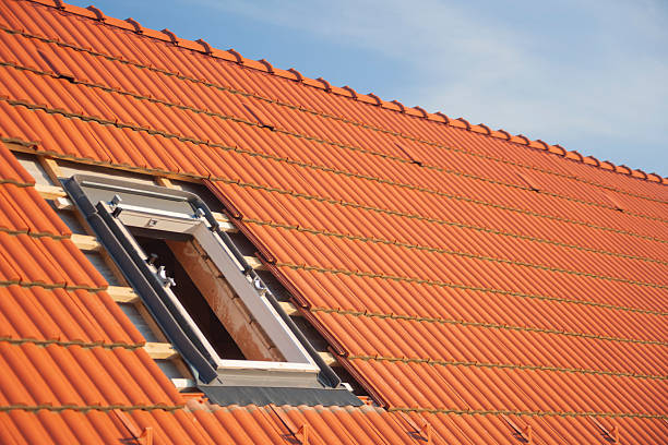 Exterior view of a roof window installed in a red ceramic tiled roof during residential house renovation. Modern skylight mounted into a pitched roof structure, providing natural daylight and improved energy efficiency. Concept of roofing, attic conversion, home improvement, construction technology, and modern architecture. Ideal for advertising campaigns, real estate marketing, renovation services, roofing companies, and building industry websites.