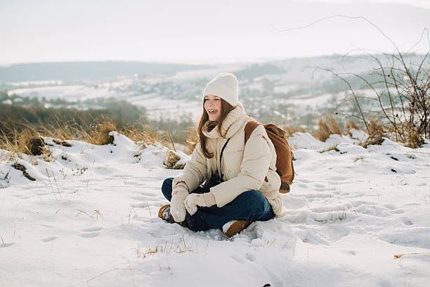 Smiling young daughter sitting cross-legged in snow, enjoying a peaceful winter day on top of a mountain with family
