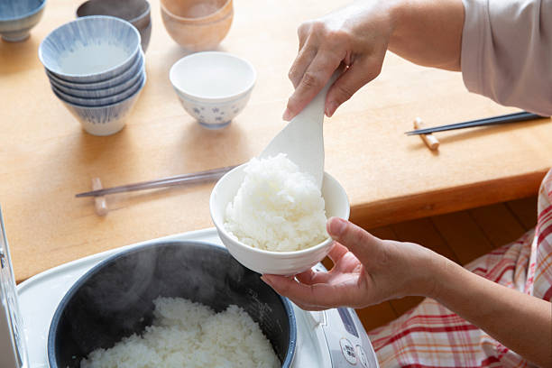 A woman's hands pouring freshly cooked rice from a rice cooker into a bowl