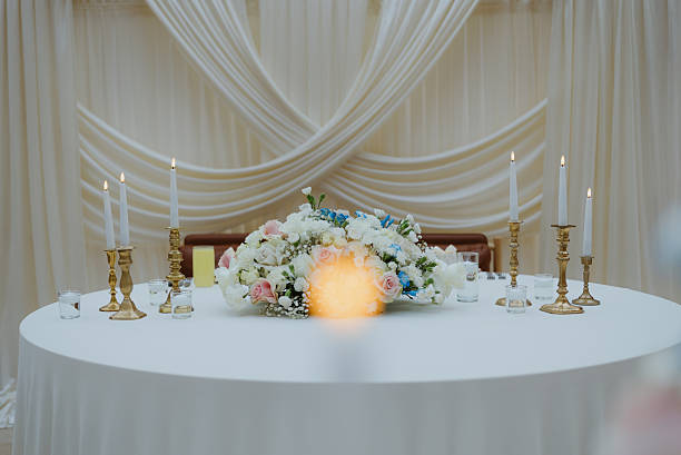 Wedding reception table with elegant white tablecloth, floral centerpiece, and lit golden pillar candle holders creating a festive ambiance