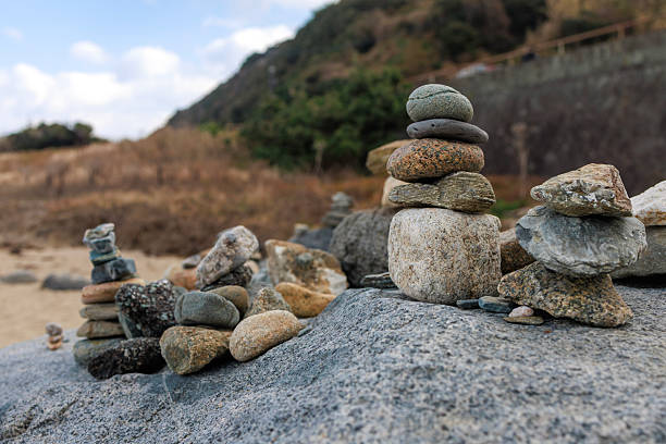 Close-up view of carefully balanced stone stacks arranged on a rocky surface near the seaside. The image symbolizes balance, mindfulness, and tranquility, set against a natural coastal landscape with soft background blur.