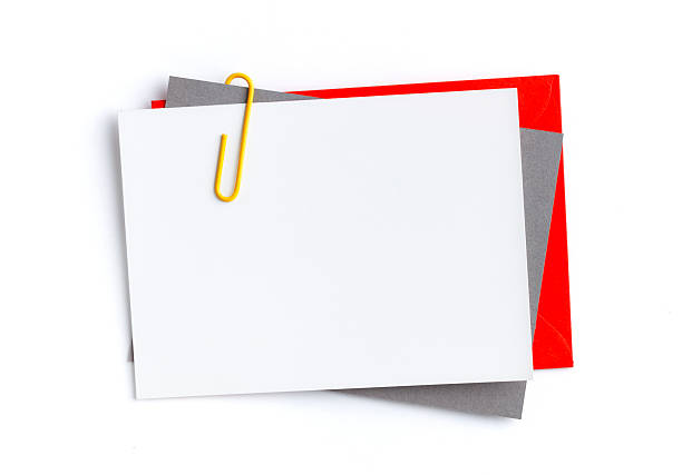 Blank greeting card layered with grey sheet and red envelope. Held together by yellow paperclip. Isolated on white background, perfect for invitations, corporate messages or holiday greetings