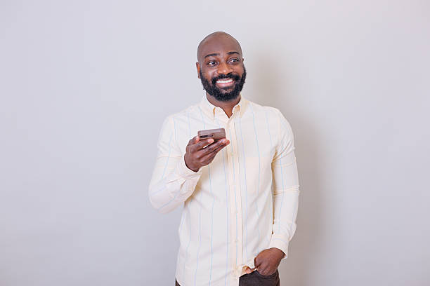 istock Smiling black man holding a smartphone, looking away happily while interacting with the device against a neutral background 2259385782