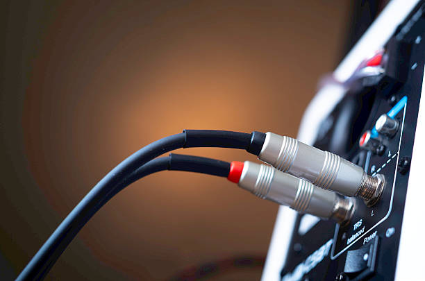 A detailed view of an audio patch panel installed in a recording studio wall, with a 1/4 inch instrument cable plugged into one of the jacks. The wooden floor and patterned carpet add to the warm and vintage atmosphere of the space. Ideal for themes related to music production, recording environments, or audio equipment.