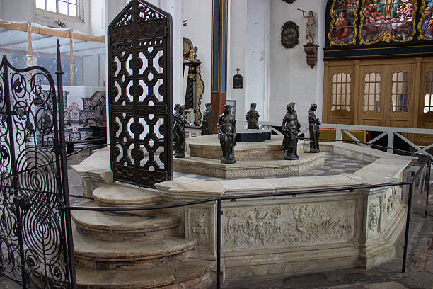 Gdansk, Poland. June 07, 2019. Historic baptismal font surrounded by sculptural figures inside church interior, presenting religious heritage and architectural details.