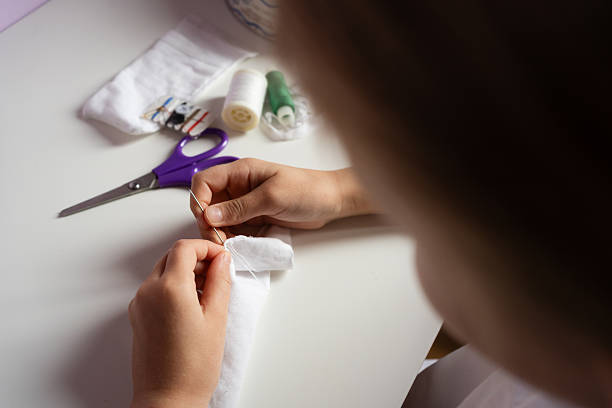 kid hands sew white fabric with a needle and thread on a light table with purple scissors and spools crafting hobby diy creative project handmade concept. High quality photo