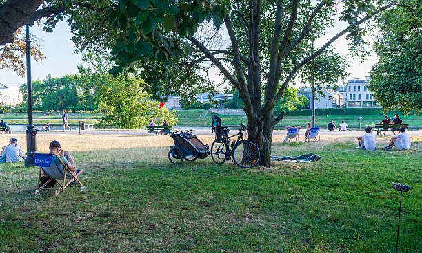 Krakow, Poland – June 29, 2025: People sit and lie on grass under large trees in a riverside park along the Vistula River, with bicycles, benches, and pedestrians visible in the background.