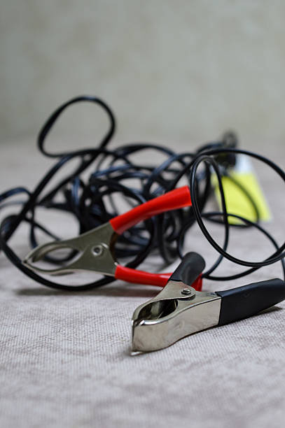 Portable LED lamp with power clips and cable on neutral background. Car repair tool, emergency lighting, automotive equipment, and DIY workshop concept.
