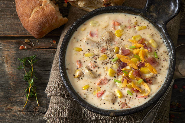 Creamy corn and potato chowder served in a white bowl and garnished with bacon, shredded cheddar cheese, and fresh herbs. A hearty homemade soup with a rich texture, styled for a comforting and satisfying meal.