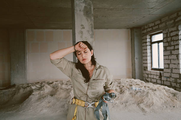 Beautiful woman at the construction site. A pretty brunette in a gray jumpsuit stands in front of a column. A female portrait without retouching with her natural imperfections