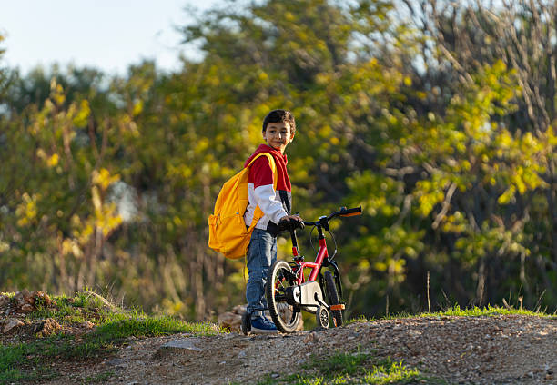 Little schoolboy with yellow backpack riding his bicycle to school