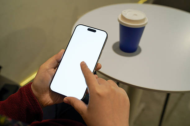 istock Person using smartphone with blank white screen beside takeaway coffee cup on table, representing mobile technology, app usage, digital lifestyle, online interaction, and modern workspace concept. 2259437683
