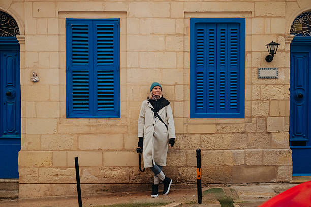 A woman leaning on a traditional Maltese facade in a historic city.