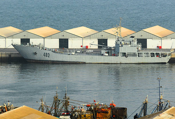 Agadir, Souss-Massa, Morocco: The RMNS Daoud Ben Aicha, identified by hull number 402, is a Champlain-class (BATRAL) landing ship tank (LST) of the Royal Moroccan Navy, pictured at the Port of Agadir. Built in France by Chantiers Dubigeon and commissioned in 1977, this 80-meter vessel is designed for amphibious operations, capable of beaching to deliver troops, vehicles, and up to 400 tons of matériel directly to shore. The ship features a distinctive bow ramp for unloading and a landing deck at the stern for light helicopters. It plays a role in Moroccan logistics, regional transport, and maritime security within the Atlantic coastal region. The vessel is armed for self-defense with 40mm anti-air guns and 12.7mm machine guns.