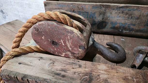 Maryborough, Australia - 4 January 2026. A worn wooden pulley with a metal hook and coarse rope lies on a timber table next to faded wooden boxes.