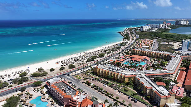 The sun has just risen over the tourist resort of Palm Beach in Aruba on the South Caribbean Sea. Several hotels and boats at anchor are seen in the image. There however, is hardly anyone on the beach as yet. Obviously it is too early. The sea is very calm. In the horizon, is an oil drilling rig. There are a few people in the image but they are too far away to be recognised. Photo shot in the early morning sunlight; horizontal format.