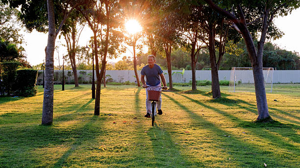 Mature man rides bicycle through tropical forest at sunset, Bangkok