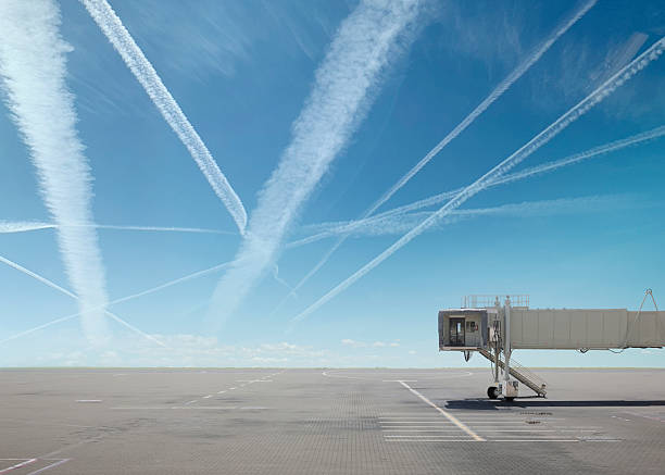 Passenger boarding bridge and empty tarmac, vapour trails above