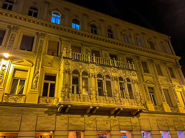 This stunning image captures the facade of a house in Budapest, beautifully illuminated by night lights. The decorative balcony elements and large windows create an enchanting scene.