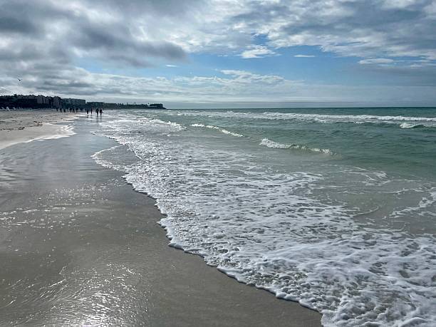 Gentle waves roll onto the shore beneath a pastel sky in this peaceful beach scene from Siesta Key, Florida. The curved coastline and distant structures hint at local life, while the natural beauty of the Gulf Coast invites quiet reflection and authentic travel moments.