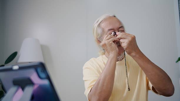 Elderly Asian man with long white hair and a mustache examines his collection of sacred Buddhist amulets while referencing information on a tablet, sipping coffee during a peaceful morning at home. A calm, wellness-inspired scene that highlights culture, mindfulness, and personal hobbies.