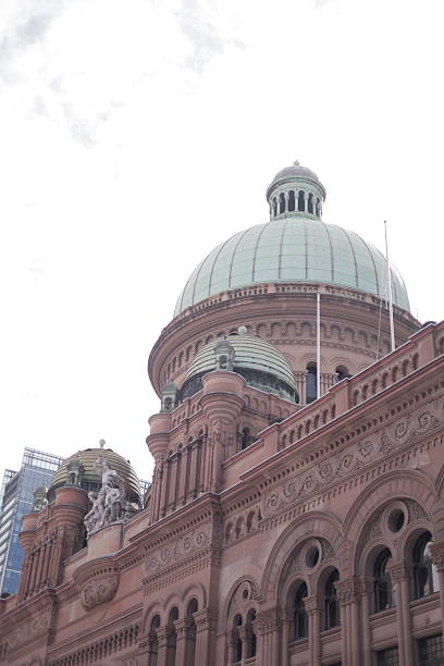 Low-angle view of the green copper-clad dome and ornate sandstone facade of the Queen Victoria Building under a bright overcast sky in Sydney, Australia.