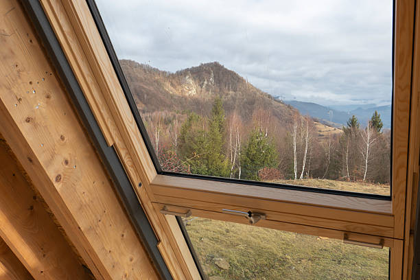 Roof window in a wooden attic interior, providing natural light and a scenic mountain view, representing modern housing, sustainable living, architecture, renovation, and home comfort concepts.