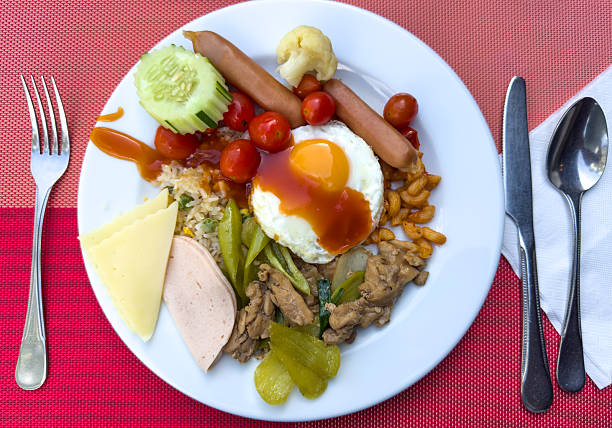 A plate of food with a fork, knife, and spoon on a table. The plate has a variety of food items such as eggs, meat, and vegetables