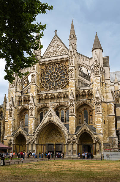 Exterior view of Westminster Abbey in London, showcasing intricate Gothic architecture, rose window, pointed arches and towering spires. Visitors explore the grand entrance, capturing a timeless historic landmark in the capital.