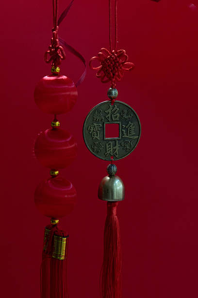 Two traditional Chinese hanging ornaments set against a rich red background. Intricately tied red knots crown glossy red beads on one charm, while the other features an ancient-style Chinese coin and a small bell, both finished with flowing red tassels.