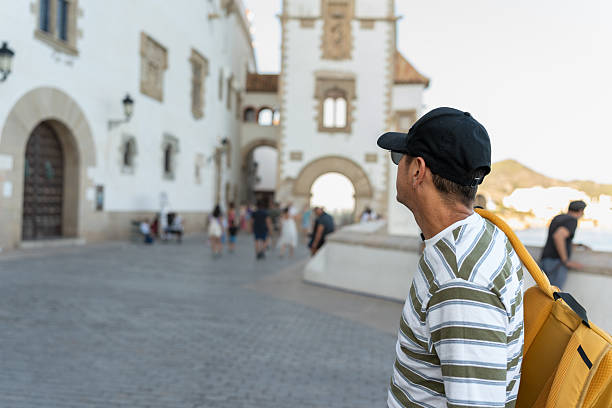 Man with a backpack looking at a historic building and tourist pathway in Sitges, Barcelona