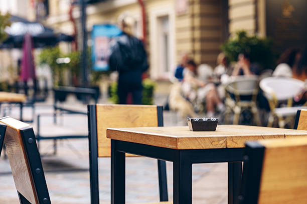 People gather and talk at outdoor tables along a busy street in warm weather.