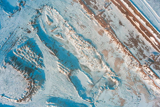 Abstract winter landscape formed by an active clay quarry covered in fresh snow. The frozen earth surface features deep ruts and mounds creating a unique industrial pattern that resembles a terraformed alien planet or Mars surface texture.