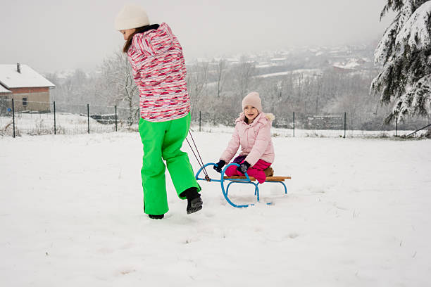 young boy and girl riding together on a sled while going downhill in a snow-covered winter park. Authentic outdoor winter activity showing childhood movement, seasonal recreation, and cold weather lifestyle in a European outdoor setting. Concept of winter activities, outdoor play, and natural leisure.