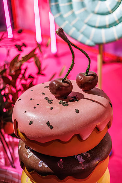 Playful stacked donut prop with pink, chocolate, and yellow glaze topped with cherries, set in a vibrant candyland-themed event space. Copy space included