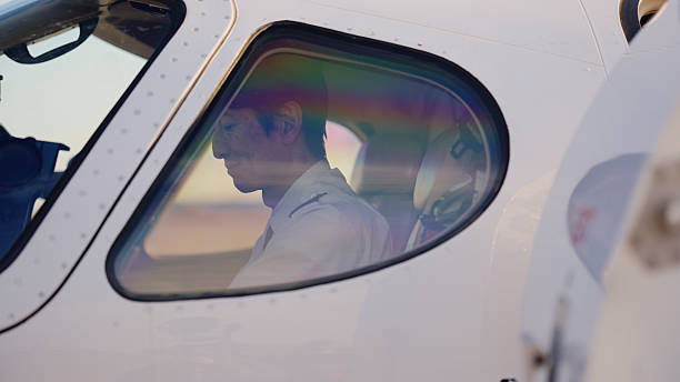 A pilot is sitting at the cockpit of a private jet and getting ready to fly. It is taken from outside of the private jet window.