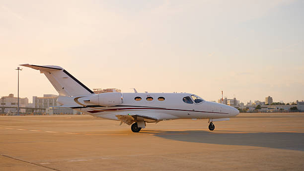 A private jet at an airport runway during sunset.
