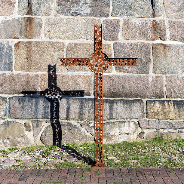 Iron cross in sunlight in front of a natural stone wall