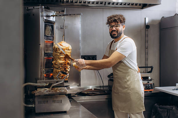 Smiling chef preparing vertical rotisserie grilled meat for middle eastern shawarma or doner kebab dish in a commercial kitchen