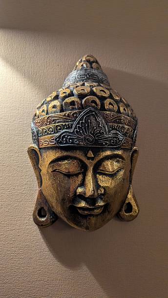 CloseUp Golden Buddha Mask On Wall, Aged Brass Patina, Carved Serene Face With Closed Eyes, Warm Directional
