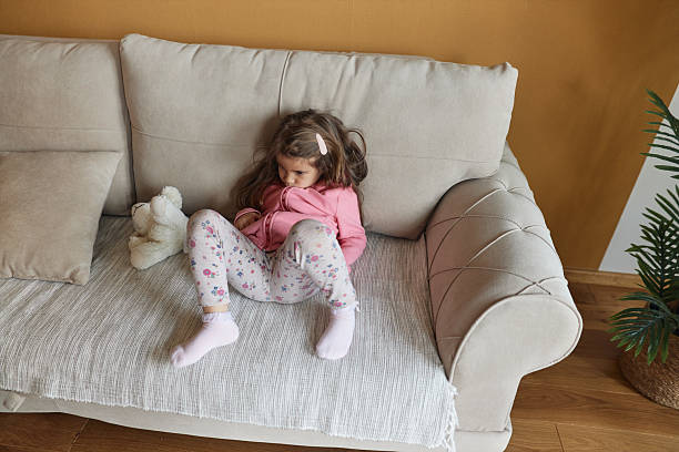 Little girl sitting on a couch with a teddy bear feeling sad