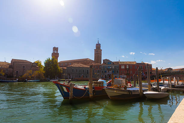 View of traditional boats moored along the waterfront in Murano, Venice, Italy. Historic buildings and calm canal waters define this quiet island scene, representing local life, travel, and the architectural character of the Venetian lagoon.