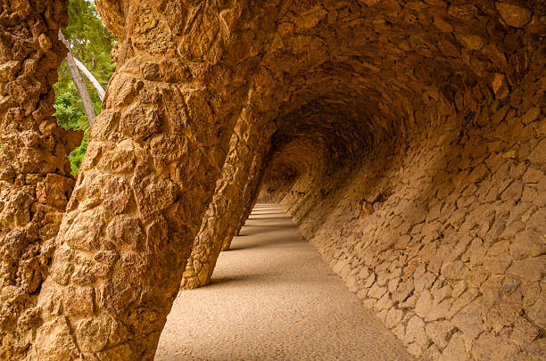 Stone archway corridor with textured walls and angled columns in Park Guell, showcasing unique architectural design and natural light.