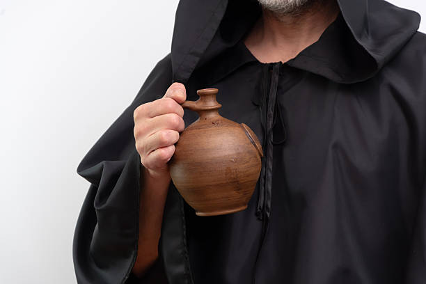 Male monk holding clay jug wearing black robe.