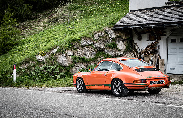 Classic Porsche 911 sports car parked on the side of the Gardena pass in the Italian Dolomites. The vehicle is stationary, showcasing its retro design and vibrant color, suggesting a moment of pause during a journey through a renowned travel destination.