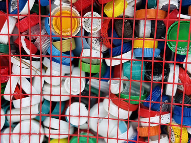 Colorful Plastic Bottle Caps In Cage Piled Inside Red Metal Mesh Collection Bin Outside Shop, Bright Lids And Mixed Materials Forming Dense Textured Pattern, Vibrant Urban Reuse Scene