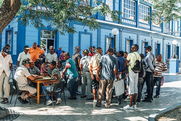 Santiago de Cuba, Cuba on February 15, 2017: A lively group of locals gathers around a wooden table on a sunny street in a blue colonial building. Friends chat, play cards, and share a moment of community in Santiago de Cuba.