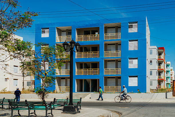 Santiago de Cuba, Cuba on February 15, 2017: Colorful blue apartment building in Santiago de Cuba, Cuba. Street life with a cyclist, pedestrians, benches and a lamp post. Bright urban setting showcasing Caribbean architecture and everyday moments.